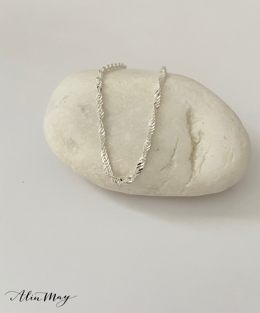 The picture shows a dainty Singapore chain necklace on a White stone