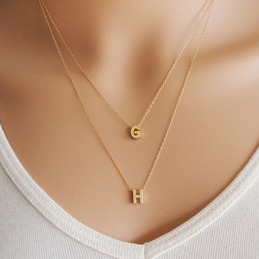 A woman is wearing two gold necklaces with a initial letter-AlinMay
