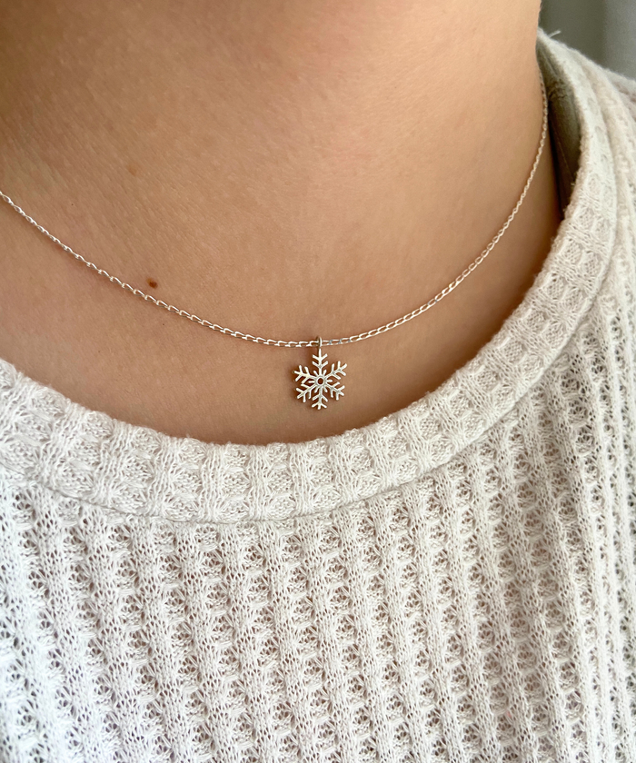 A woman wears a minimalist Sterling silver chain necklace with a dainty and shiny snowflake pendant that slides freely along.