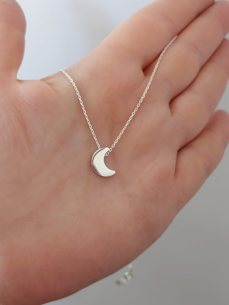 Image: A woman shows on her hand a sterling silver moon necklace in smooth and shiny finish