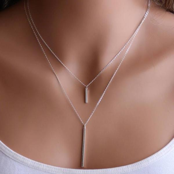A woman is wearing a small bar necklace and a long bar necklace in Sterling Silver.